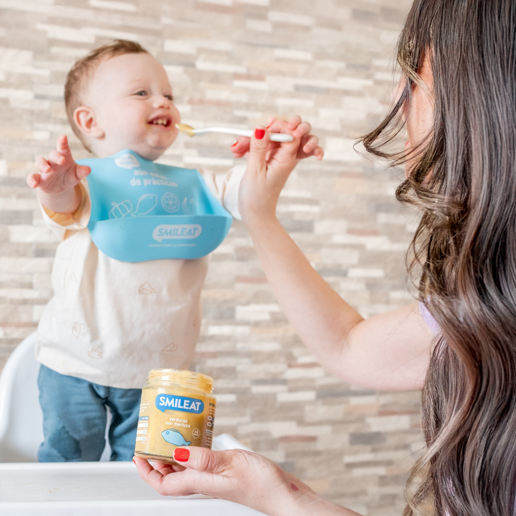 Bebé na cadeira a comer um boião biológico que a mãe lhe dá – alimentação infantil com ingredientes reais e honestos